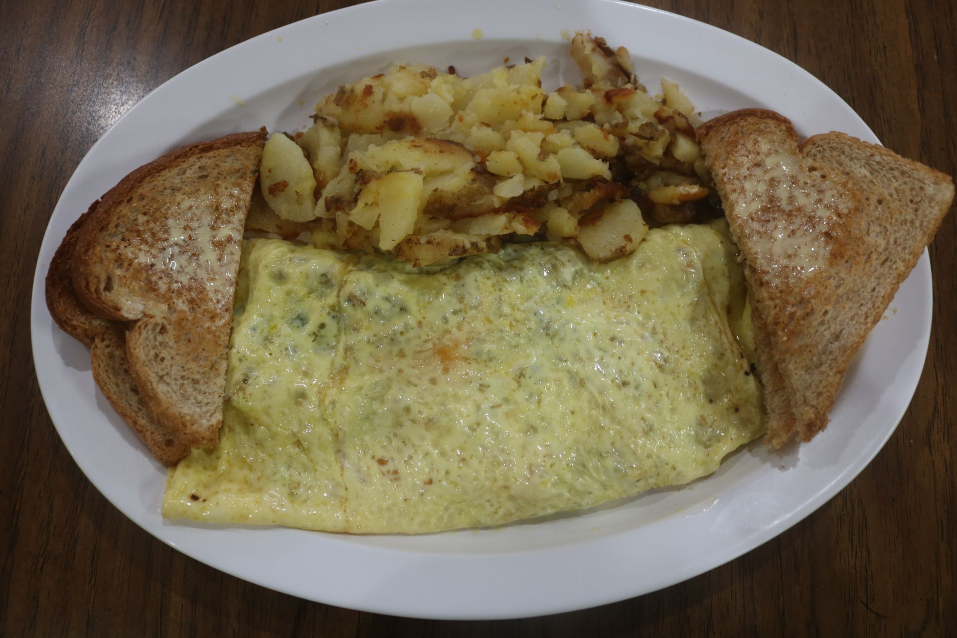 A white plate topped with an omelet , toast and potatoes.