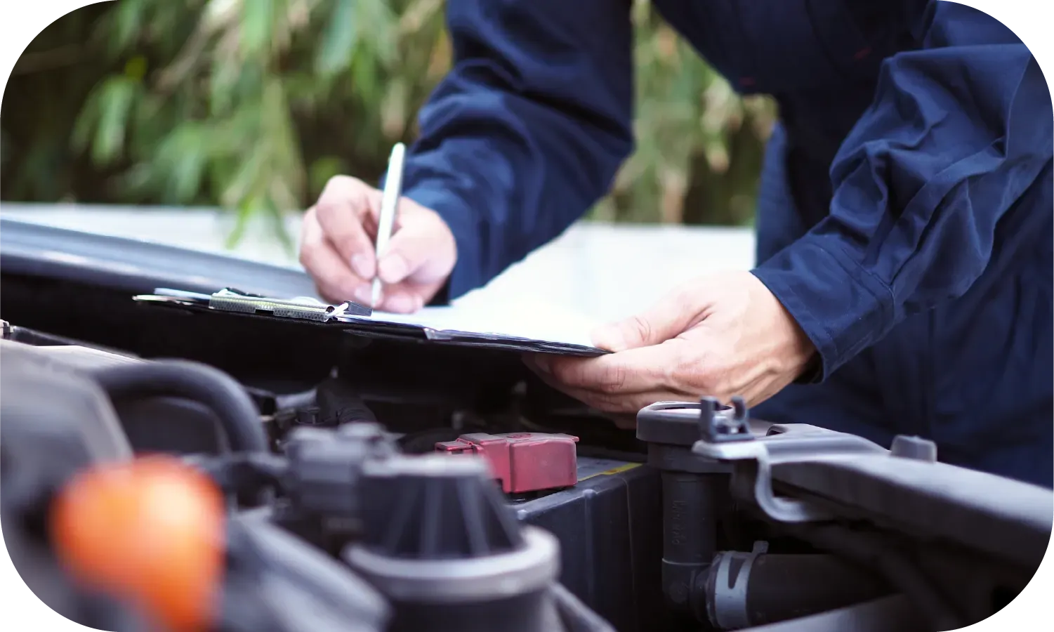 A mechanic is writing on a clipboard while working on a car.