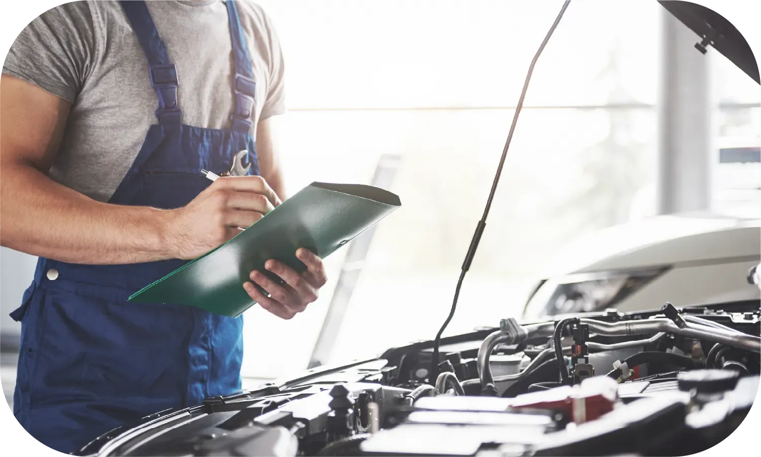 A man is standing in front of a car with the hood open and writing on a clipboard.