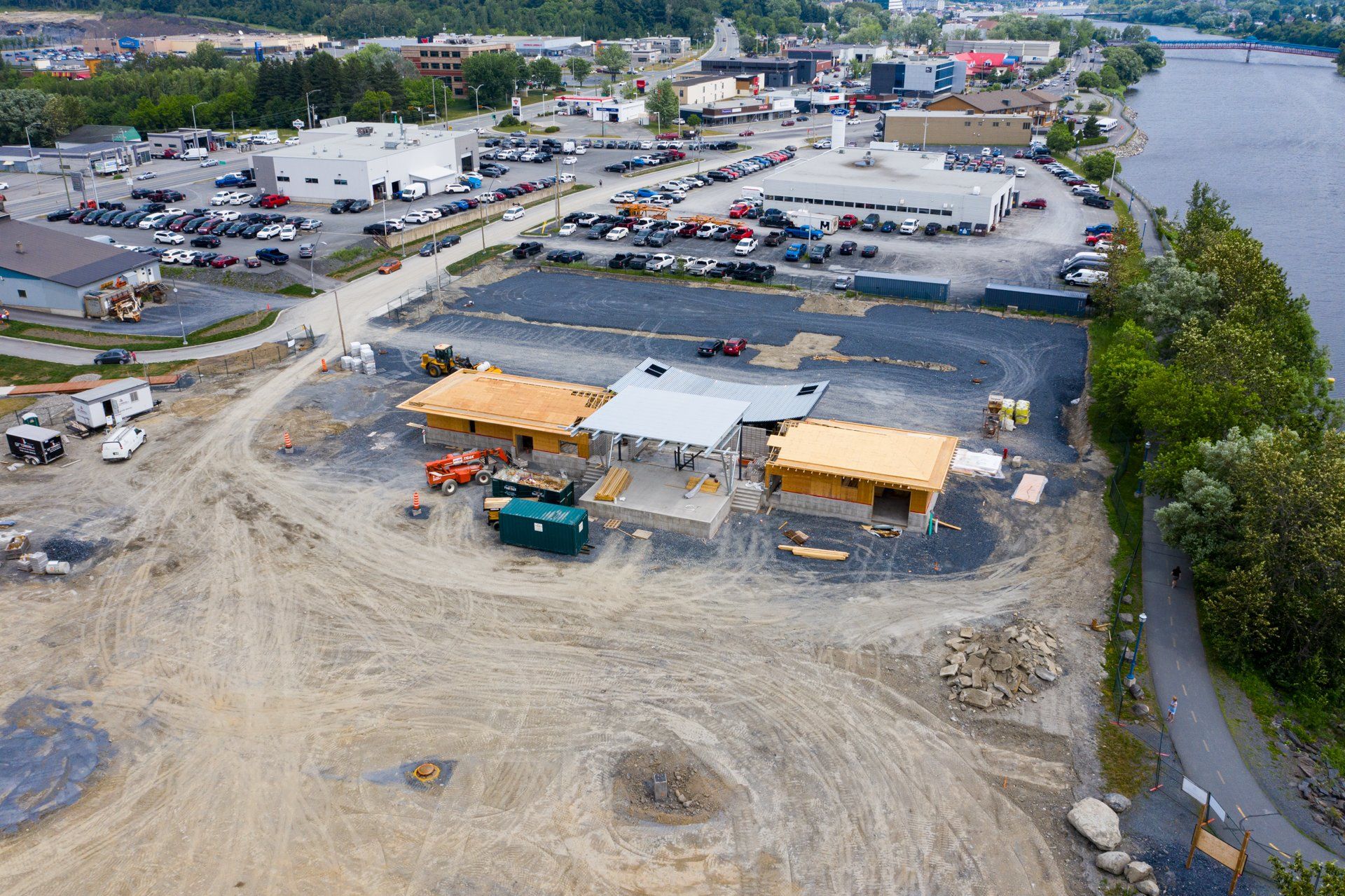 Vue aérienne d'un chantier de construction avec des structures partiellement construites, un parking et une rivière.
