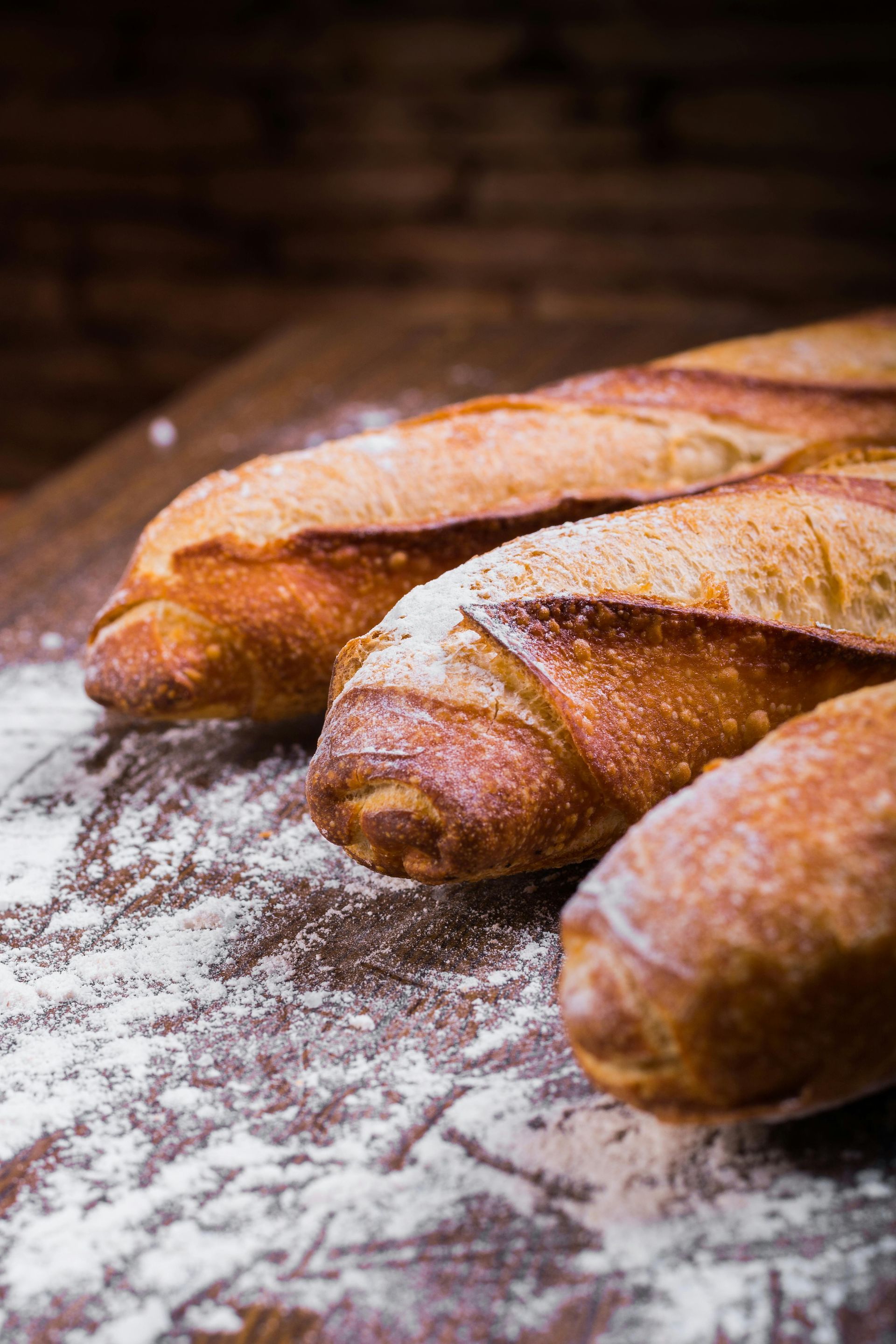 Three loaves of bread are sitting on a wooden table covered in flour.