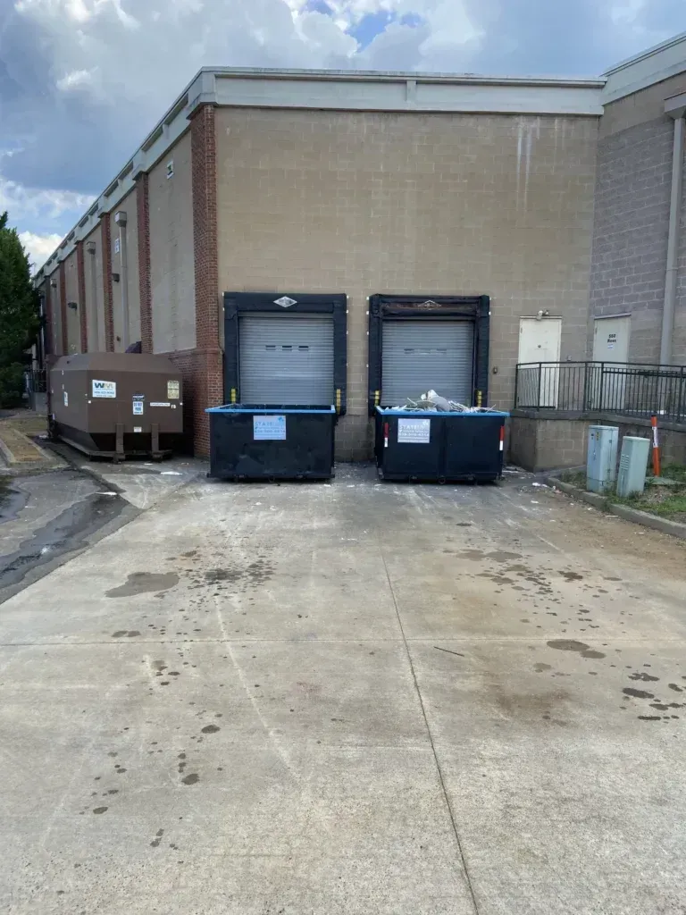 Back alley with loading docks and dumpsters in front of a brick and beige building.