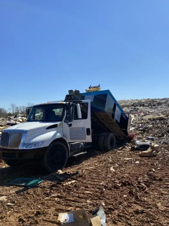 White dump truck dumping trash at a landfill on a sunny day.