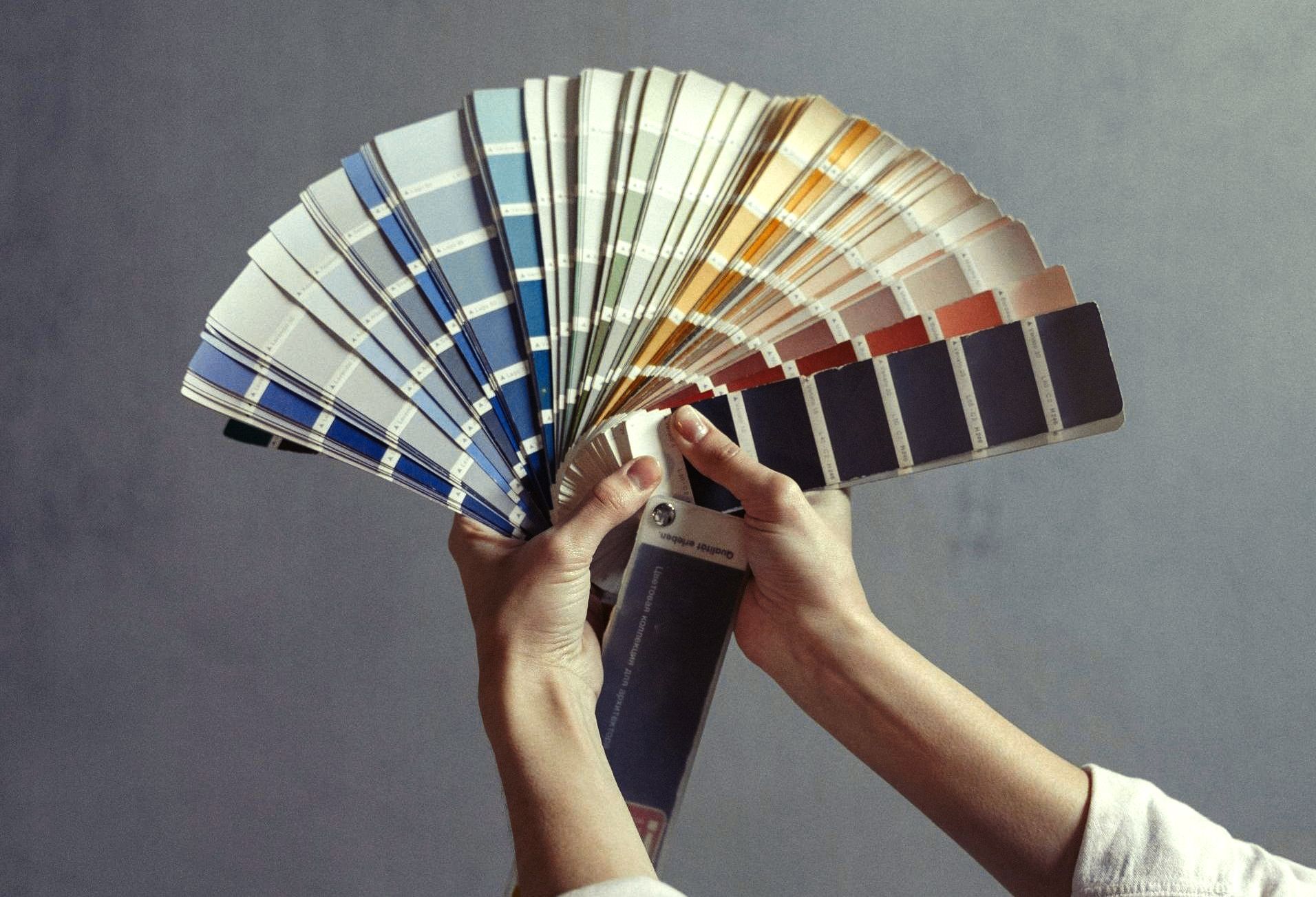 Una persona sostiene un abanico con muestras de pintura en sus manos.