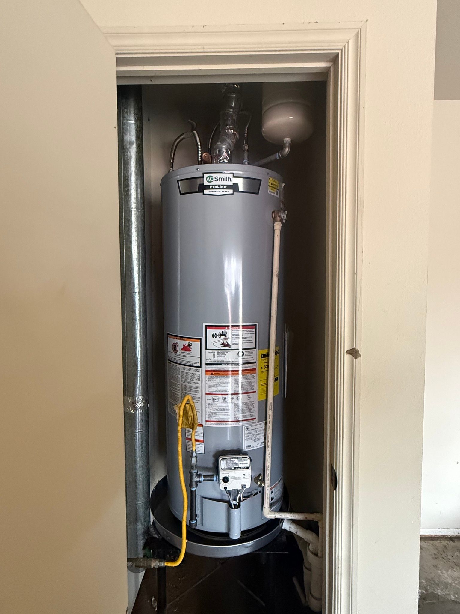 Water heater in a narrow closet, with yellow gas line and pipes visible.
