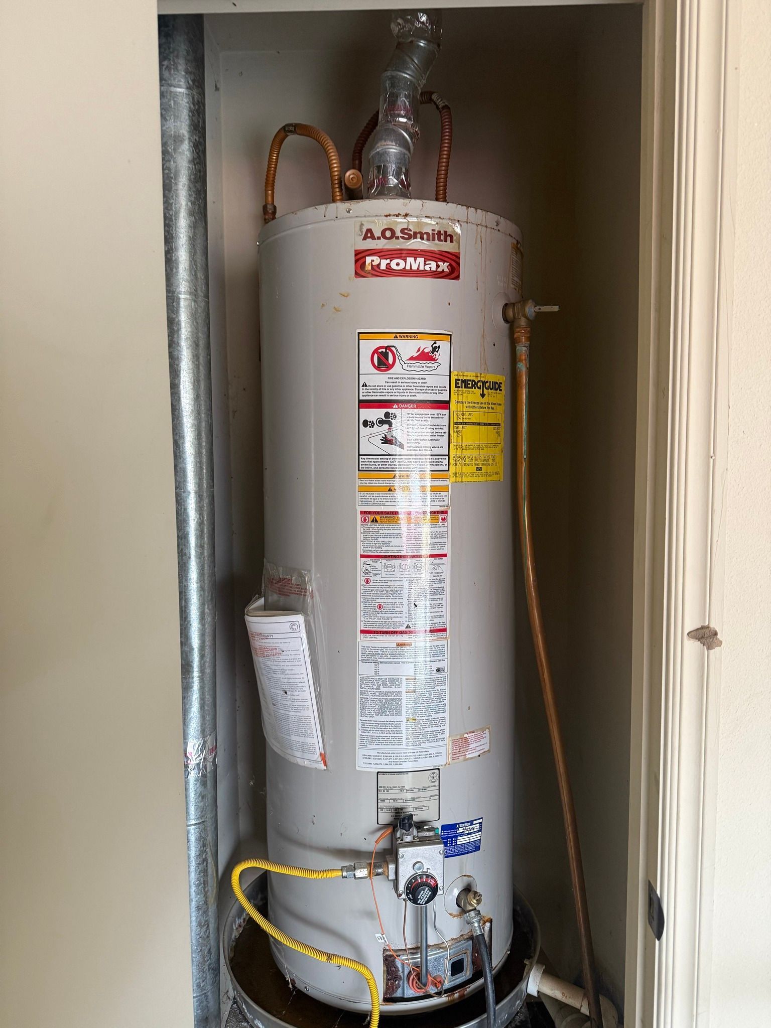 Water heater in a utility closet with pipes, valves, and warning labels.