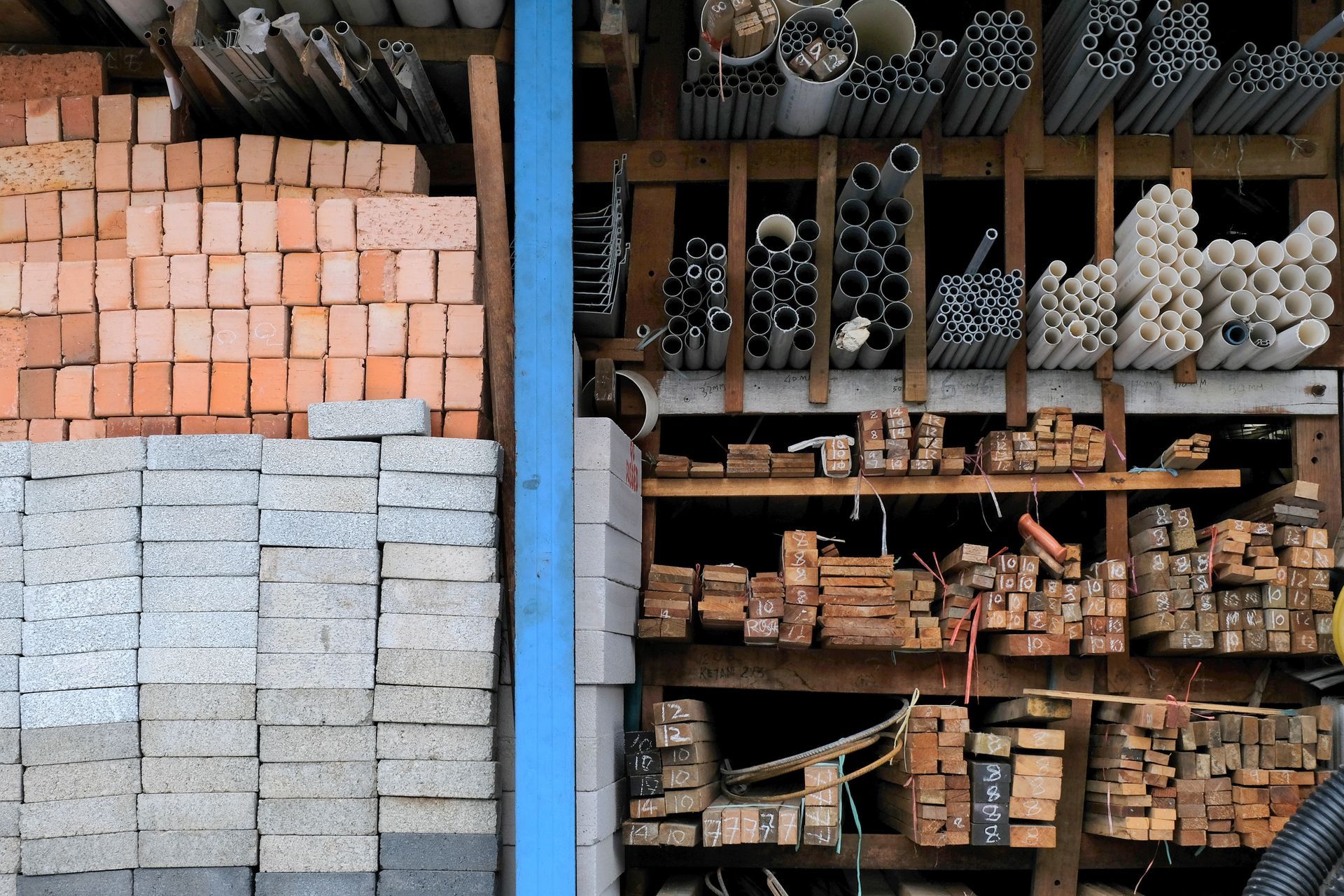 Shelves with stacked bricks, lumber, and assorted metal and PVC pipes in storage. Shelves with stacked bricks, lumber, and assorted metal and PVC pipes in storage.