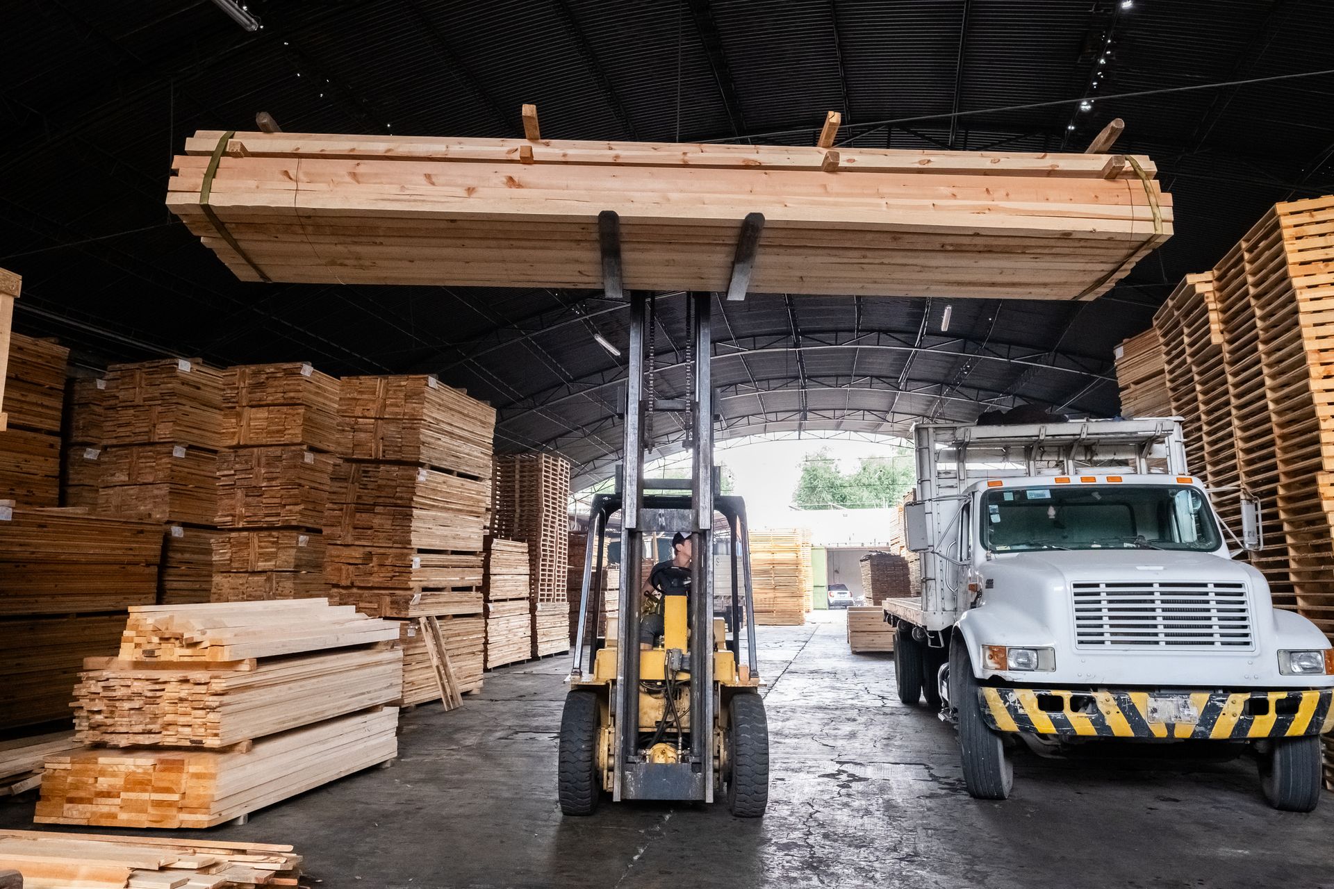 A machine next to a truck lifts a stack of wood, showcasing essential construction materials.
