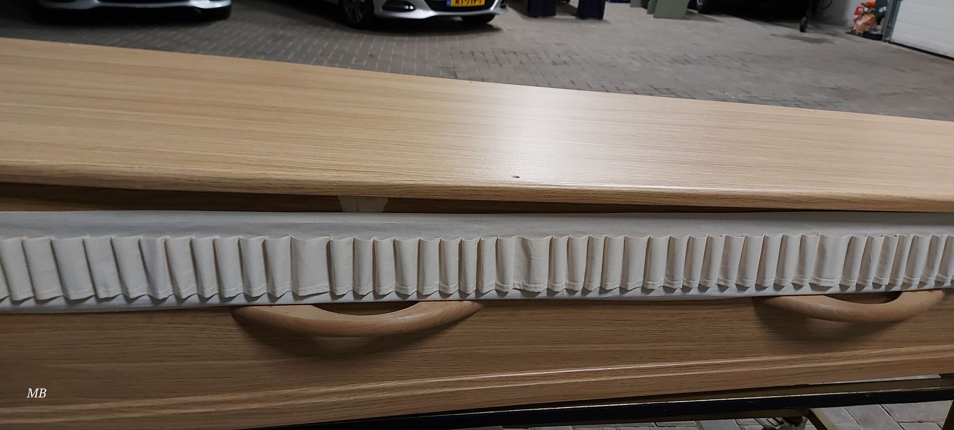 Een houten doodskist staat op een houten tafel in een garage.