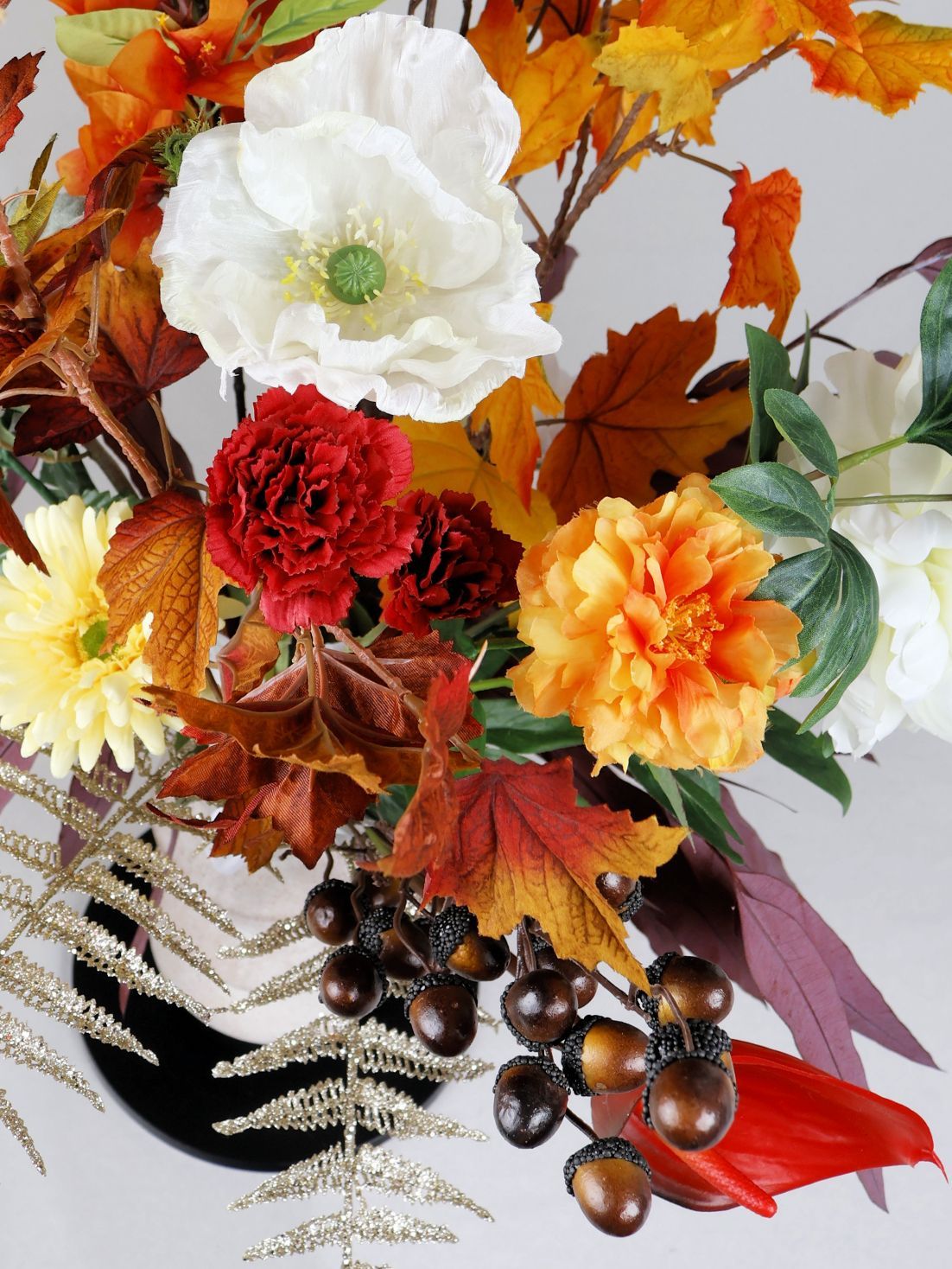 Herfstbloemstuk in een witte vaas met oranje, rode en witte bloemen en herfstbladeren.