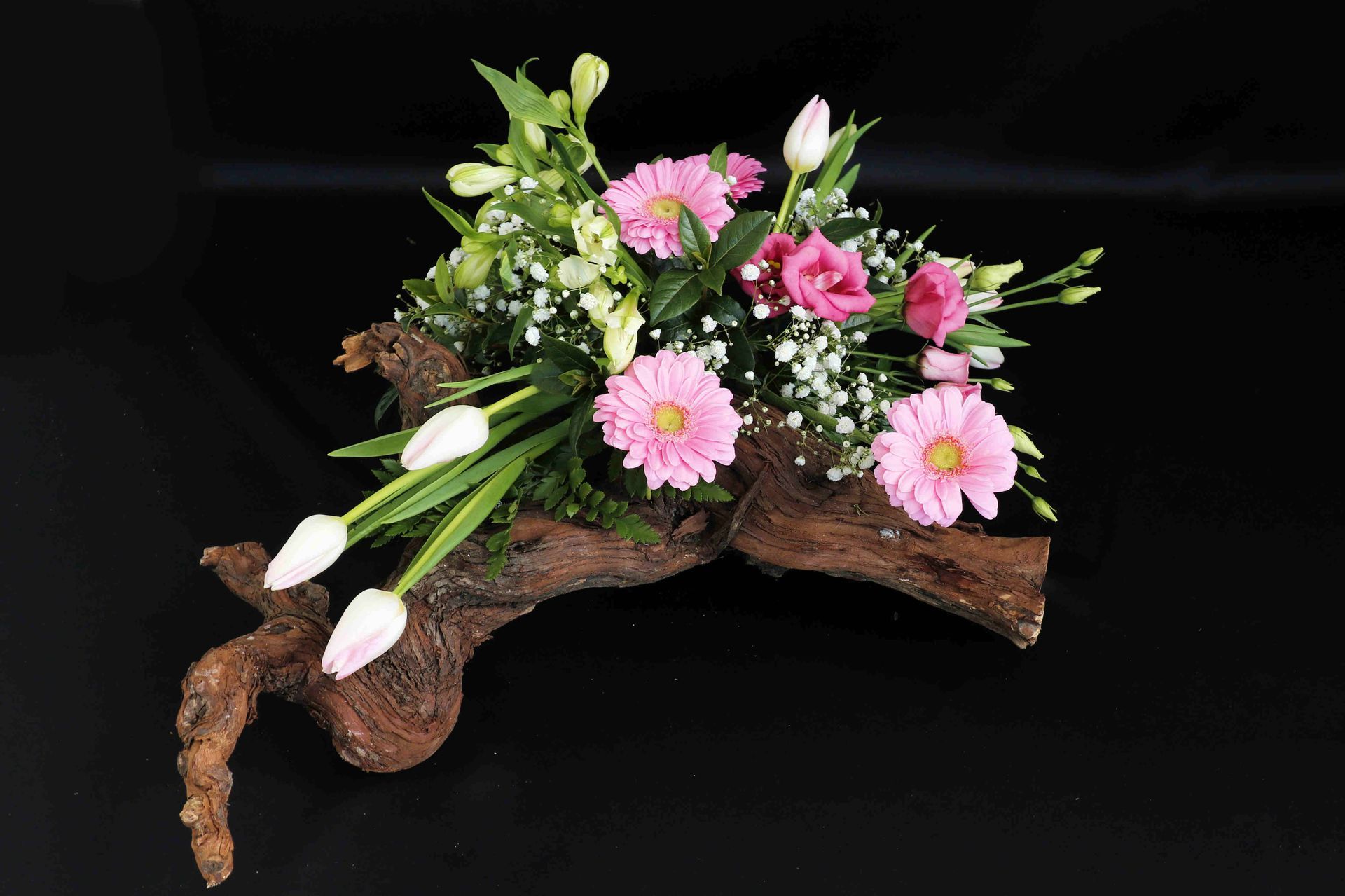 Een bloemstuk roze en witte bloemen op een stuk druivenhout