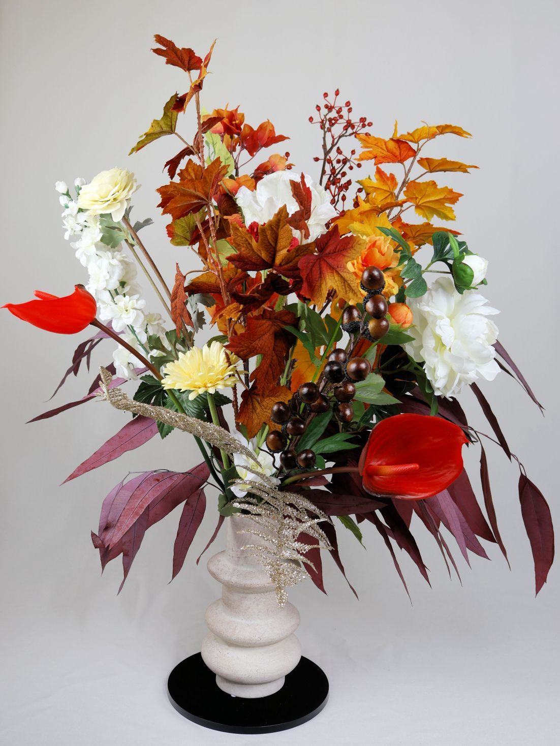 Herfstbloemen met kleurrijke bladeren, witte en rode bloemen in een crèmekleurige vaas.