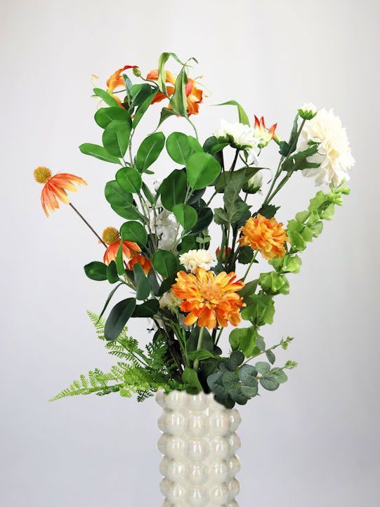 Een vaas gevuld met gele en witte zijdenbloemen op een tafel