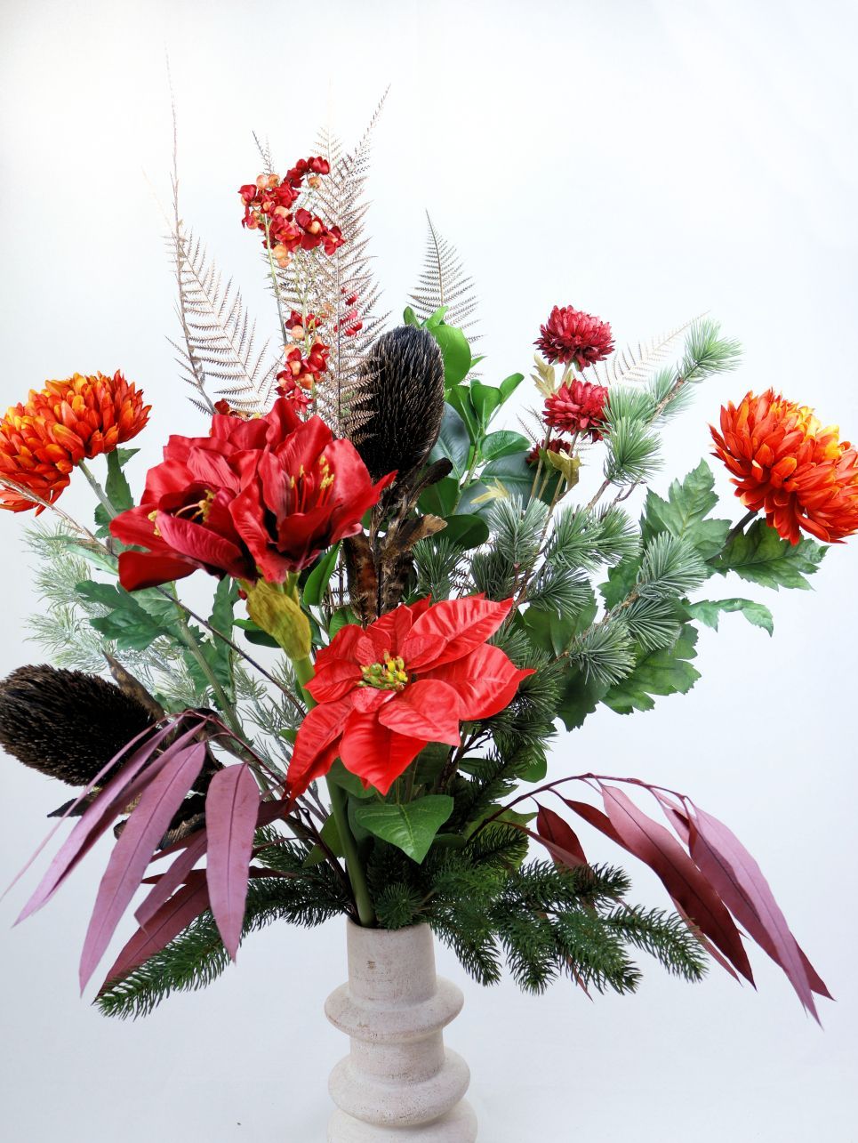 Een feestelijk bloemstuk in een vaas met rode kerststerren, oranje chrysanten en groenblijvende planten.