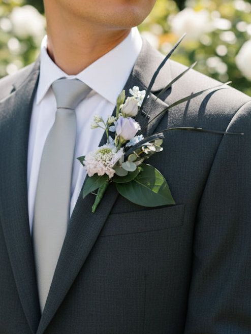 Man in grijs pak met boutonnière, lichtgrijze stropdas en wit overhemd.