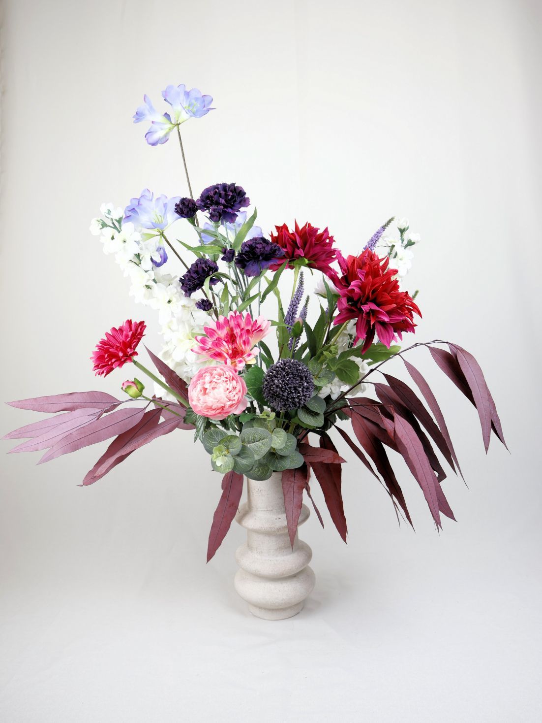 Een boeket met levendige bloemen in een crèmekleurige vaas tegen een witte achtergrond.