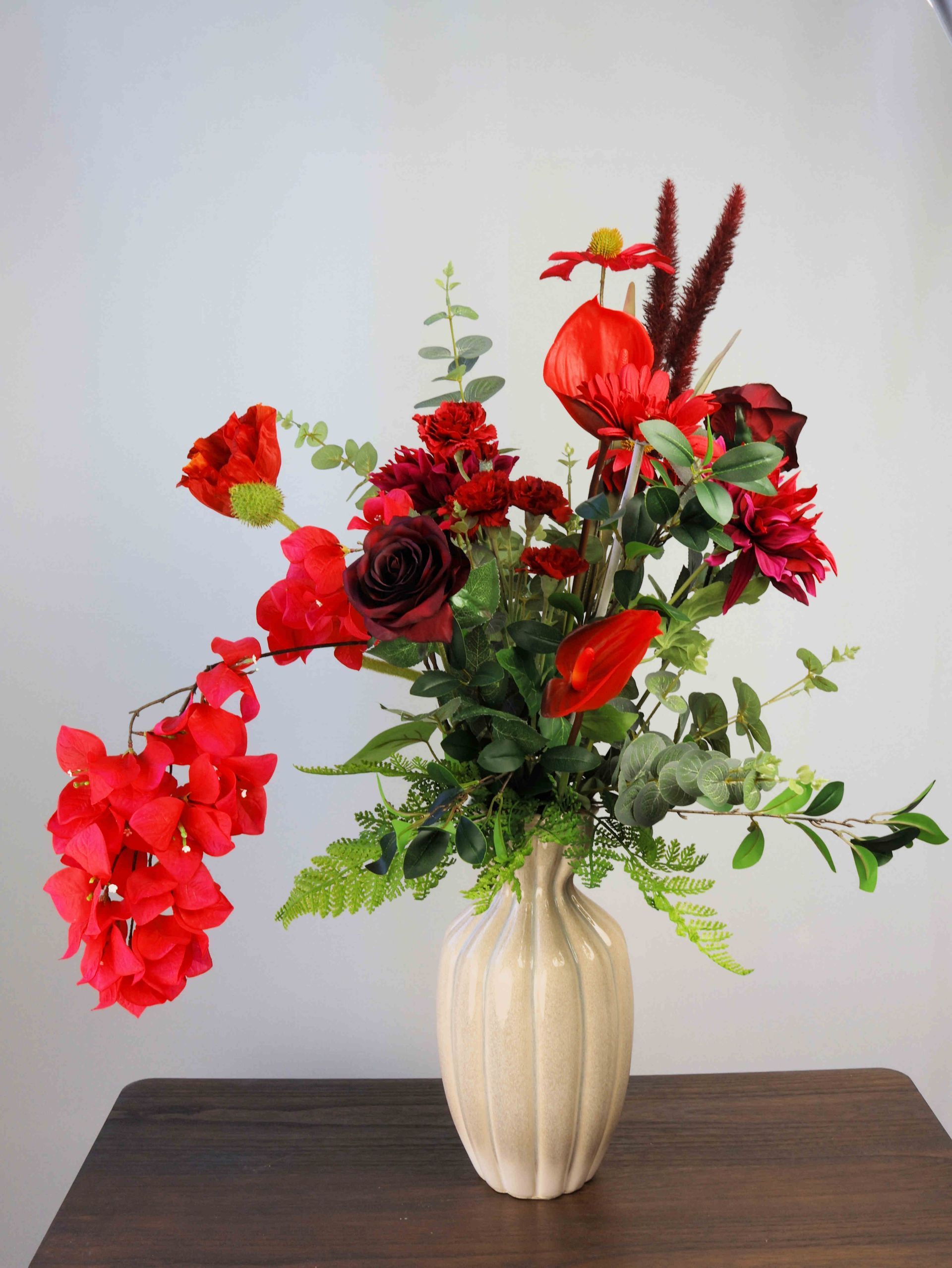 Op een houten tafel staat een vaas gevuld met rode zijdenbloemen.