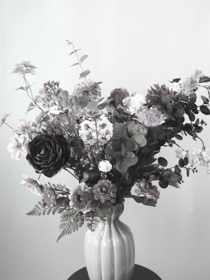 Een bloemstuk in een zwarte vaas op een houten tafel, naast een raam.