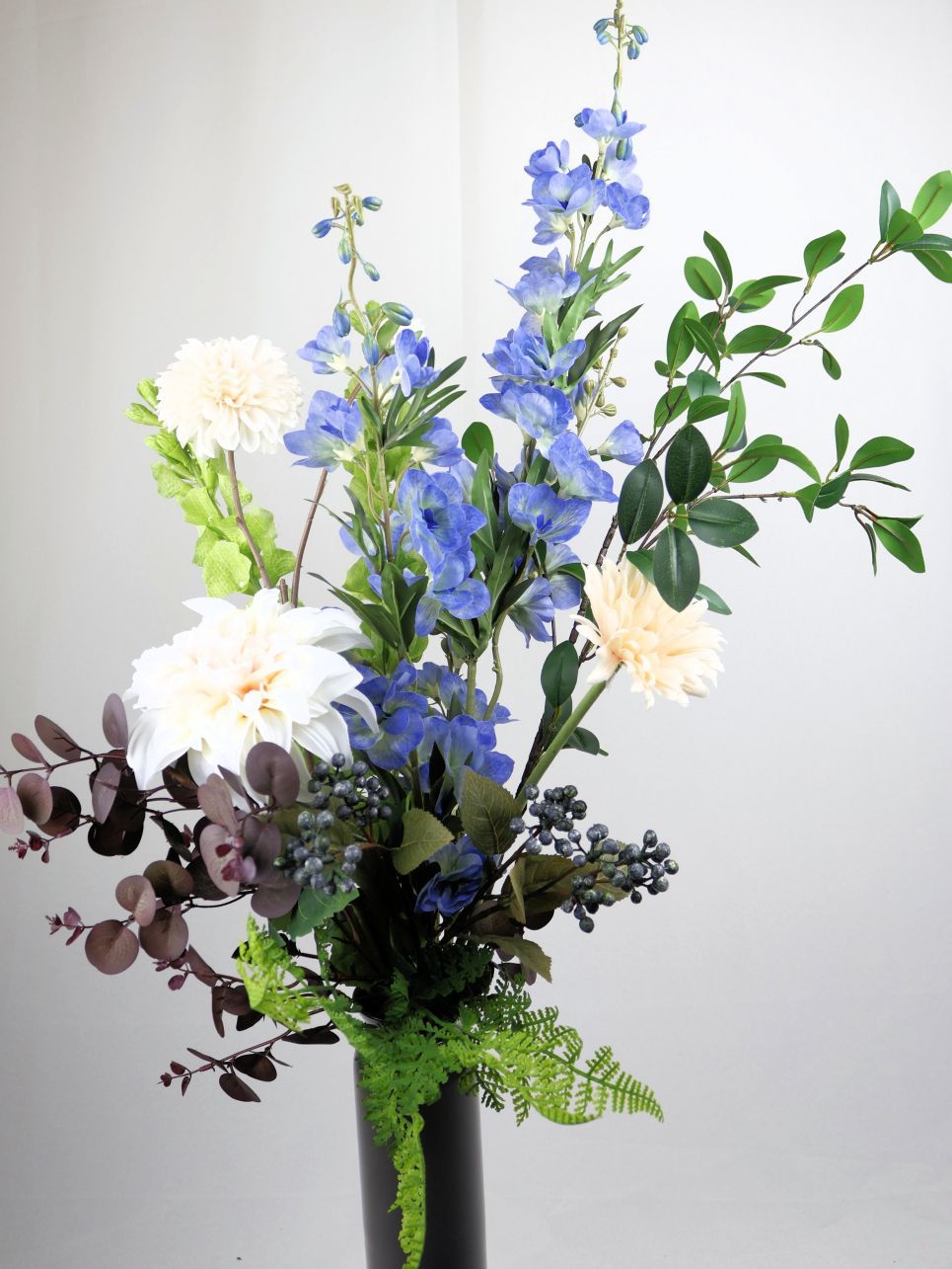 Blauwe en witte bloemen in een zwarte vaas, met groen en paars bladgroen.