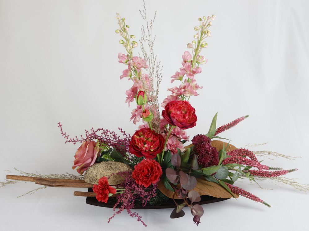 Kleurrijk zijdenbloemen in een groene vaas op een zwarte tafel tegen een witte achtergrond.