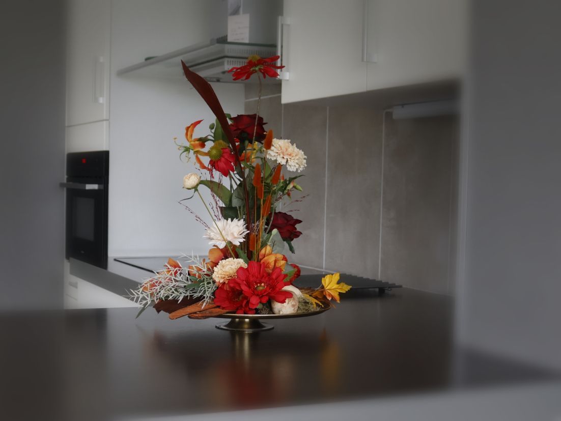 Kunstig bloemstuk op een aanrecht in de keuken; rode, oranje, witte en groene bloemen.