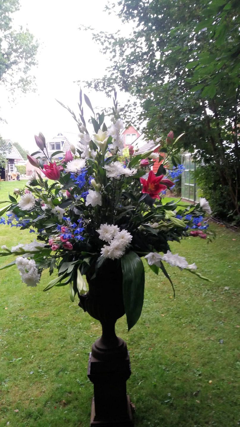Bloemstuk in een donkere urn op een groen gazon, met kleurrijke bloemen en weelderig bladgroen.