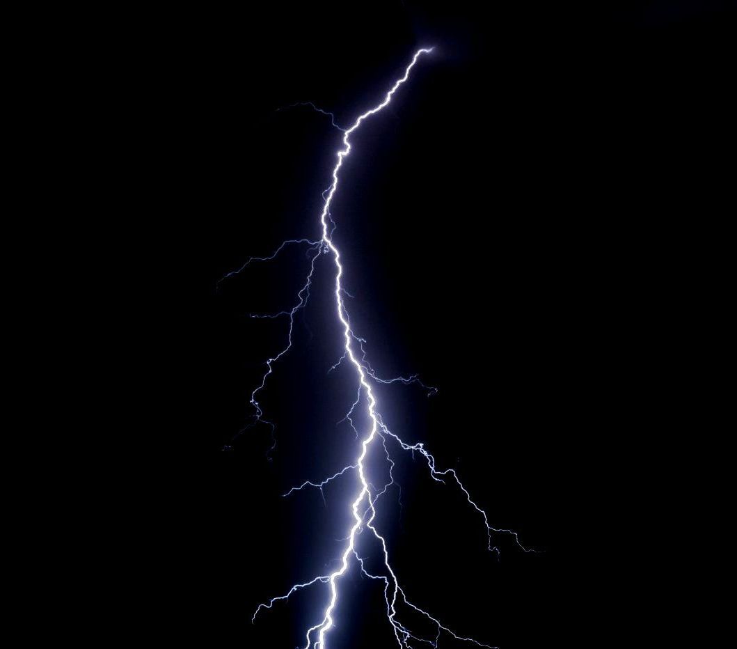 A lightning bolt is strikes in the dark sky.