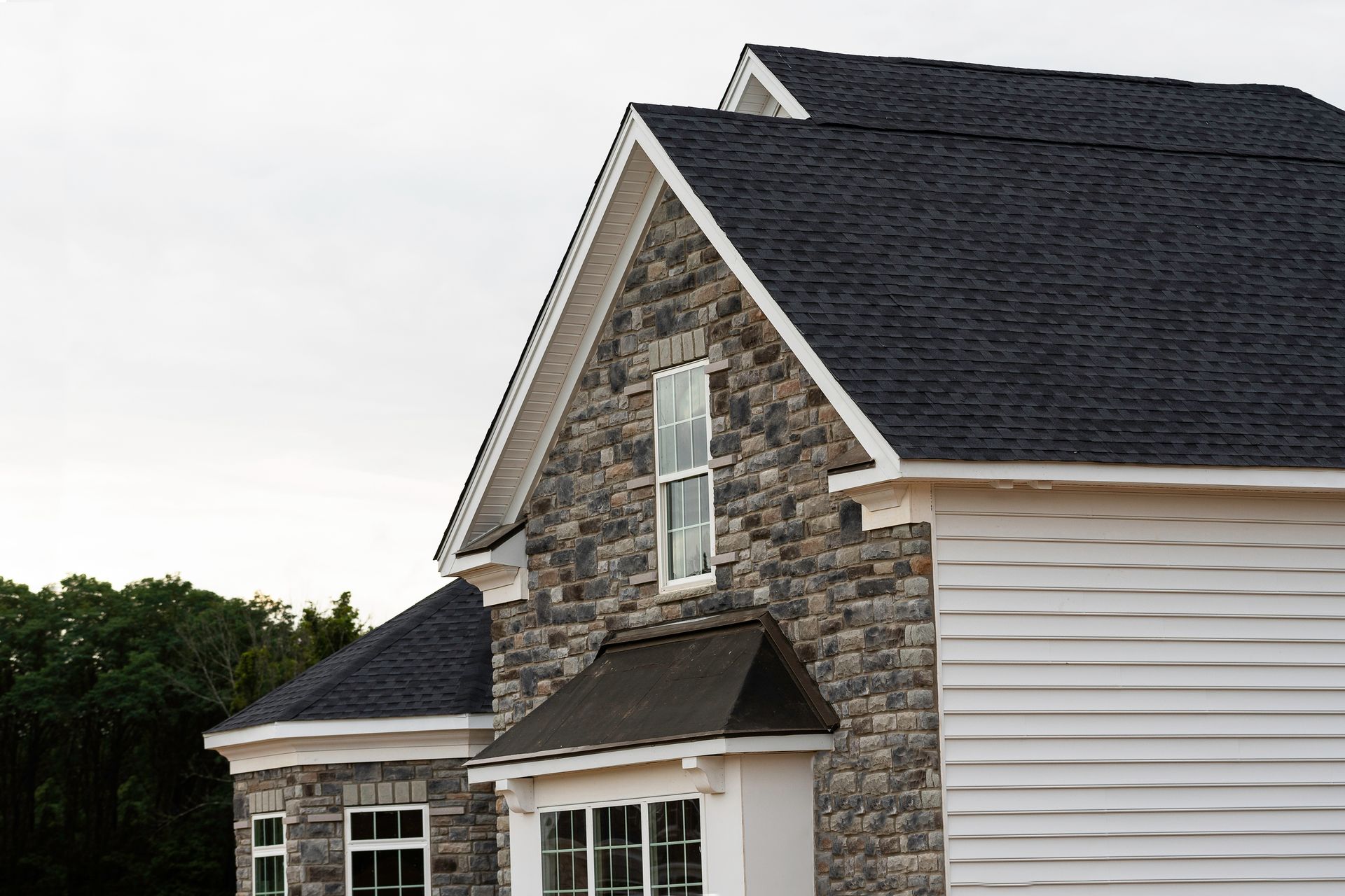 A stone house with a black roof and white siding
