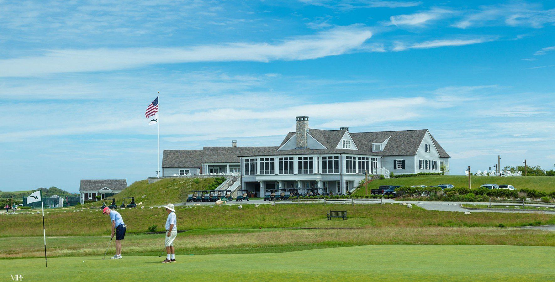 A man is putting a golf ball on a green in front of a large house.