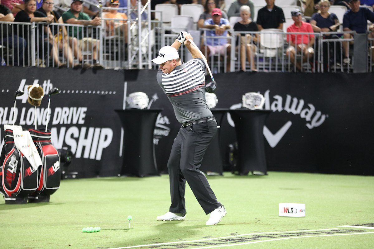A man is swinging a golf club in front of a sign that says world long drive championship