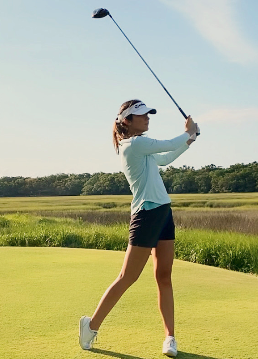 A woman is swinging a golf club on a golf course.