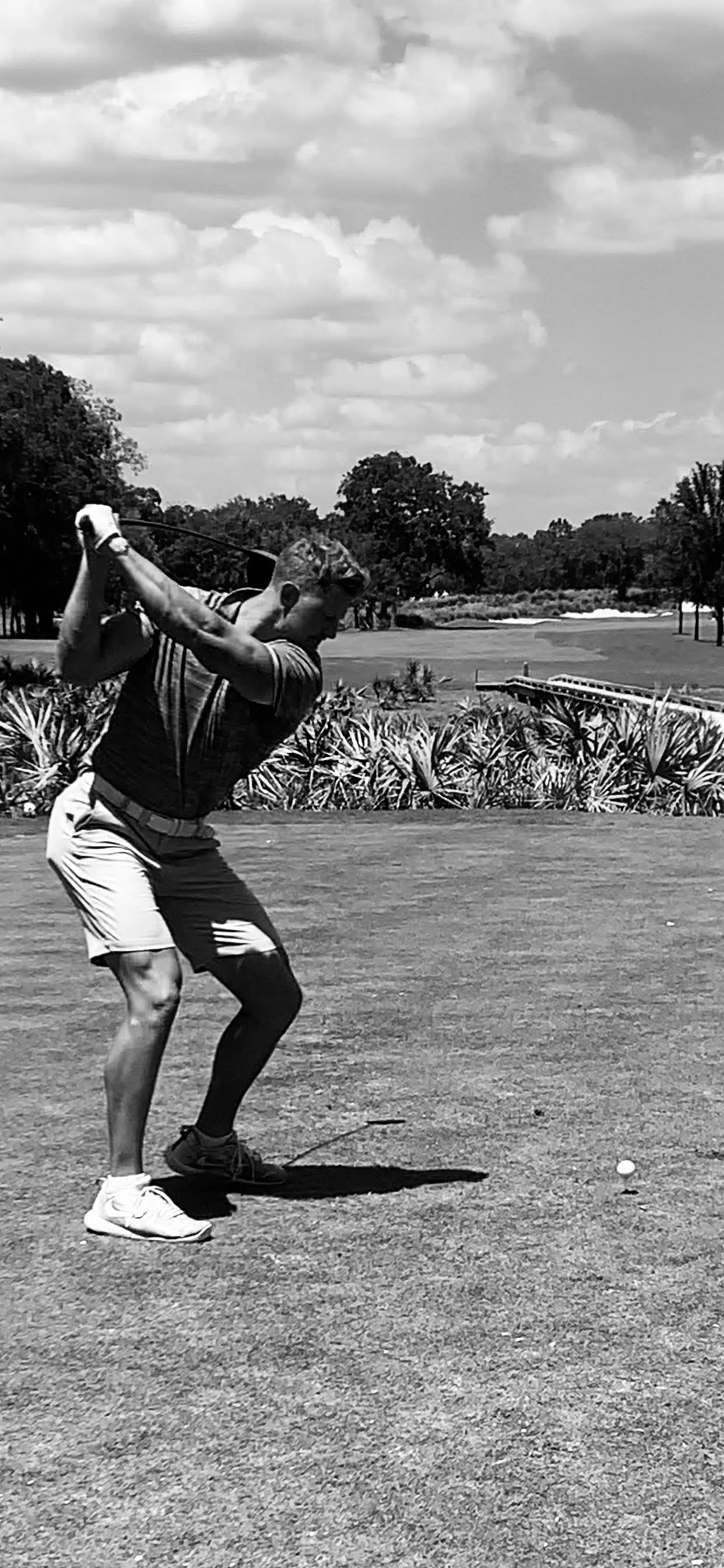 A person swinging a golf club on a grassy golf course, in black and white.