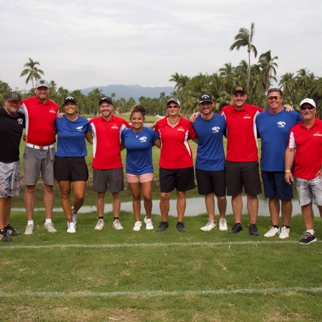Group of people in red and blue shirts standing on a golf course with arms around each other.