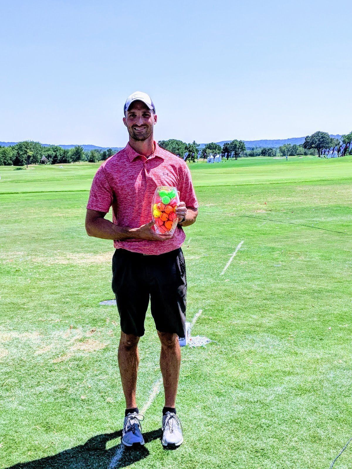 A man is standing on a golf course holding a jar of golf balls.