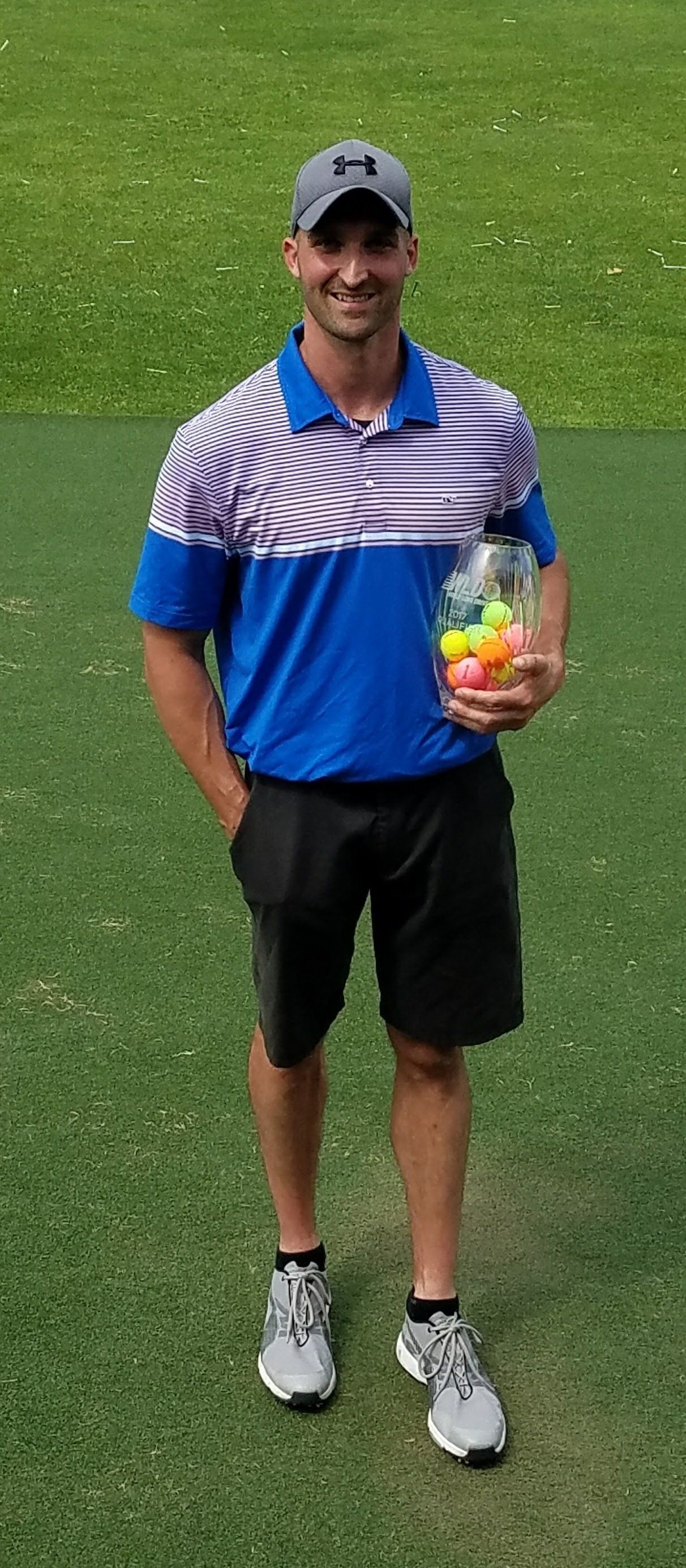 A man in a blue shirt and black shorts is holding a bag of golf balls.