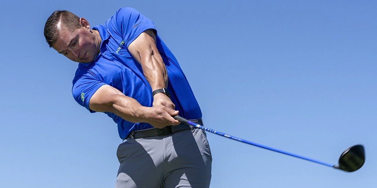 A man in a blue shirt is swinging a golf club on a golf course.
