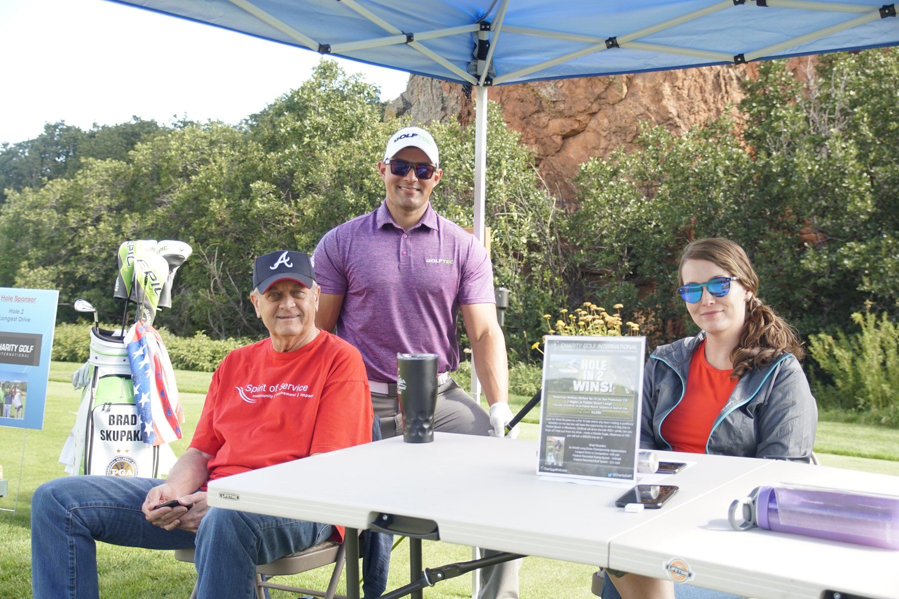 A group of people are sitting at a table under a blue tent.
