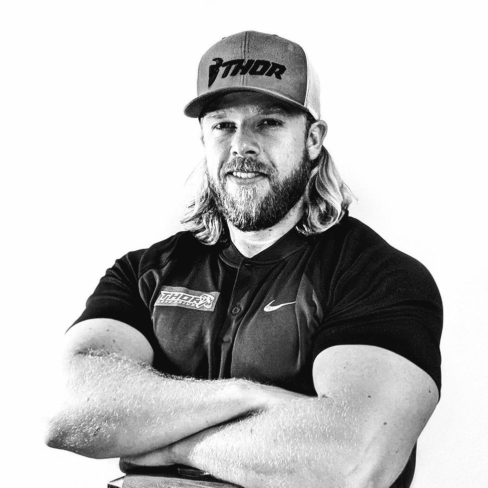 A man with a beard and a hat is standing with his arms crossed.