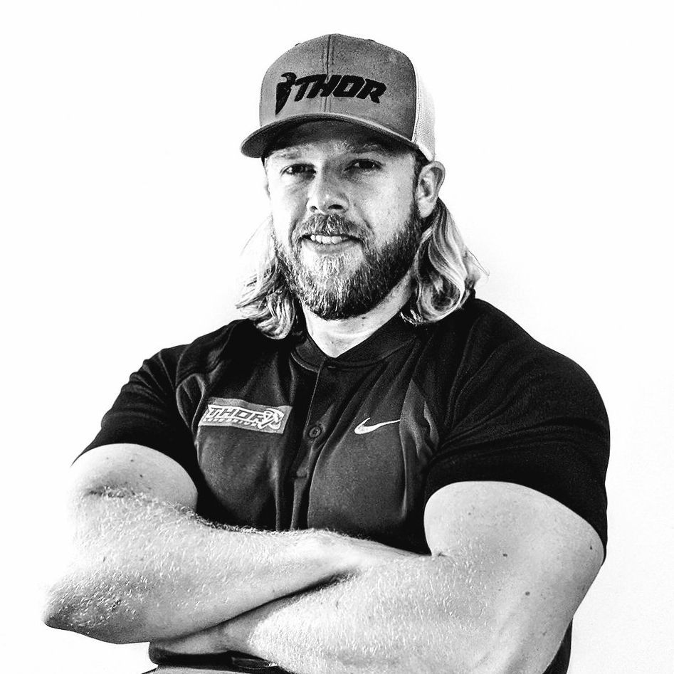 A man with a beard and a hat is standing with his arms crossed.