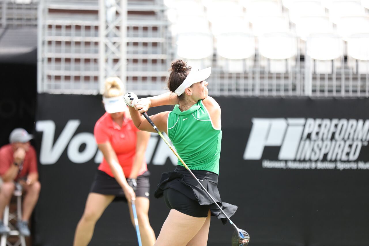 A woman in a green shirt is swinging a golf club