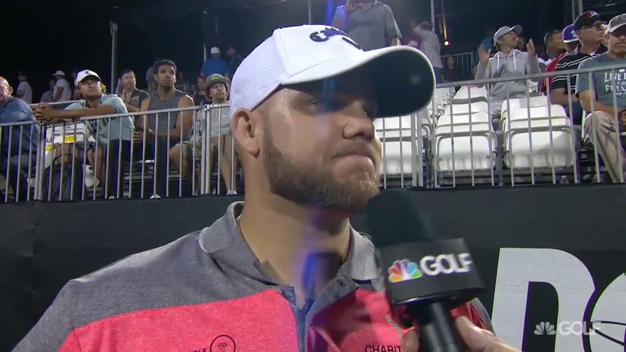 Man in hat being interviewed on a golf course at night, holding a microphone.