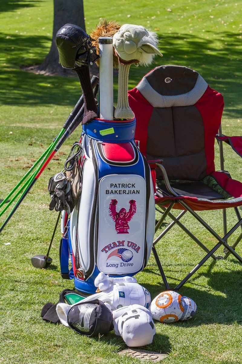 Golf bag with clubs, Yoda and BB-8 headcovers, Team USA logo, red and blue chair on grass.