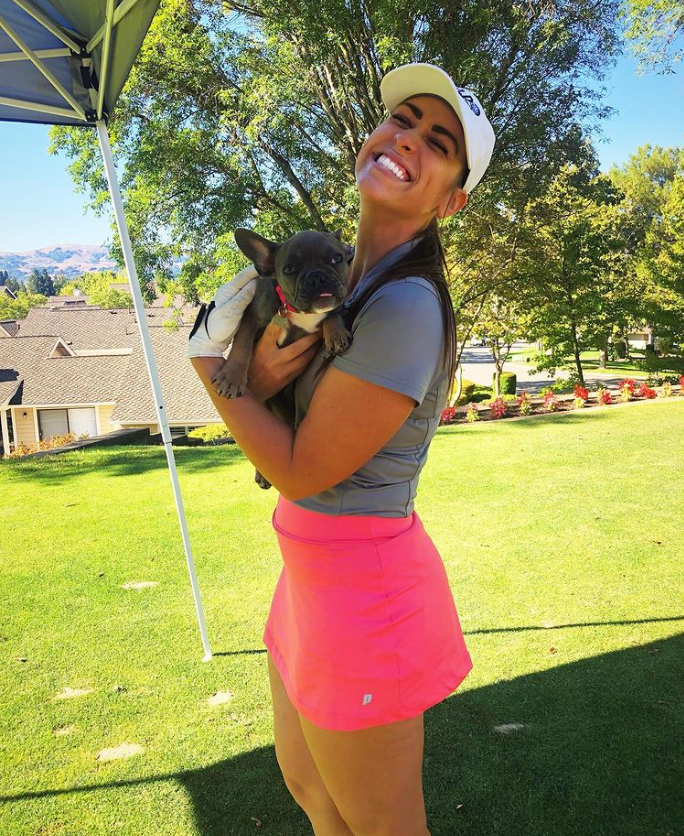 A woman is holding a small dog on a golf course.