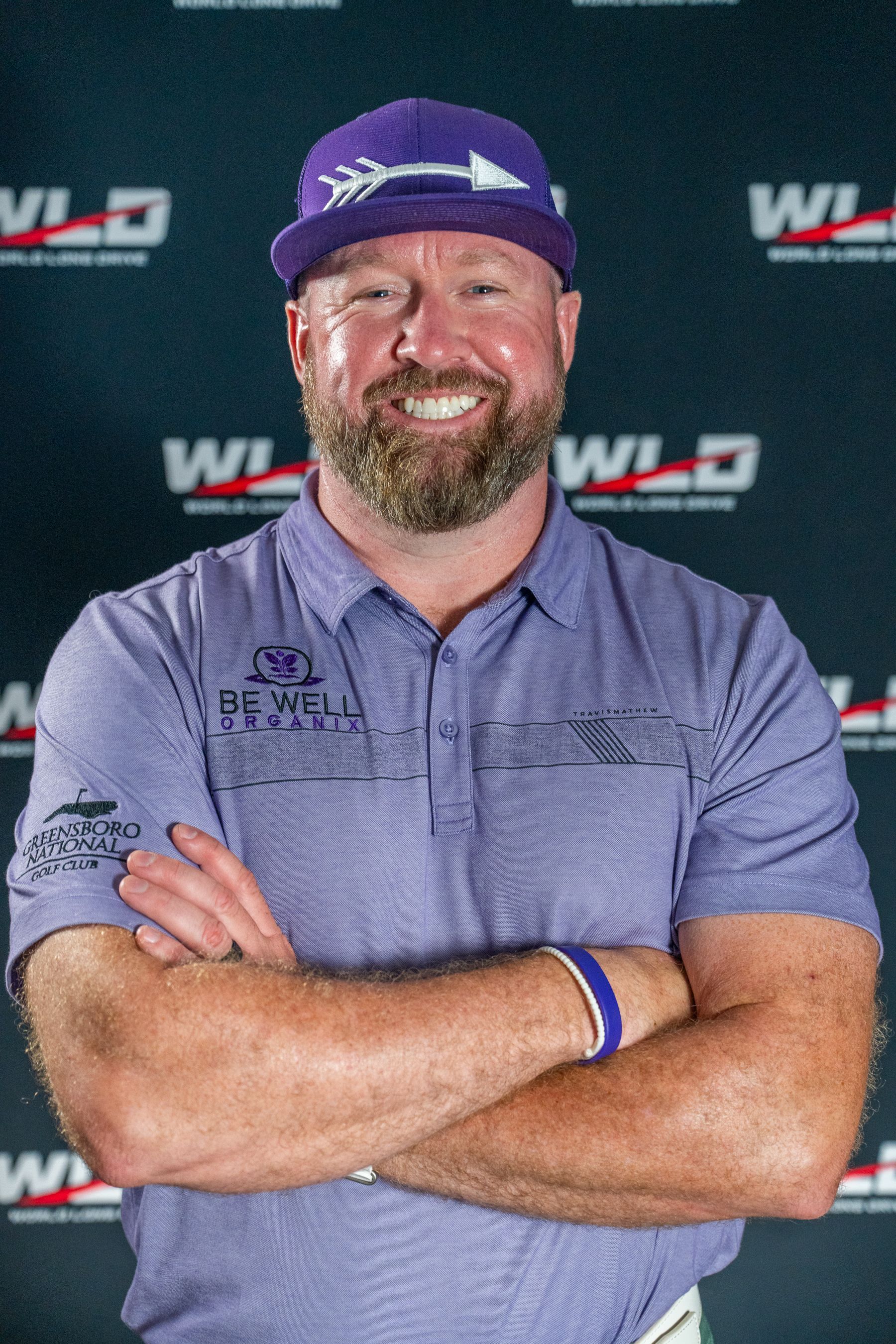 A man wearing a purple hat and a purple shirt is standing with his arms crossed.