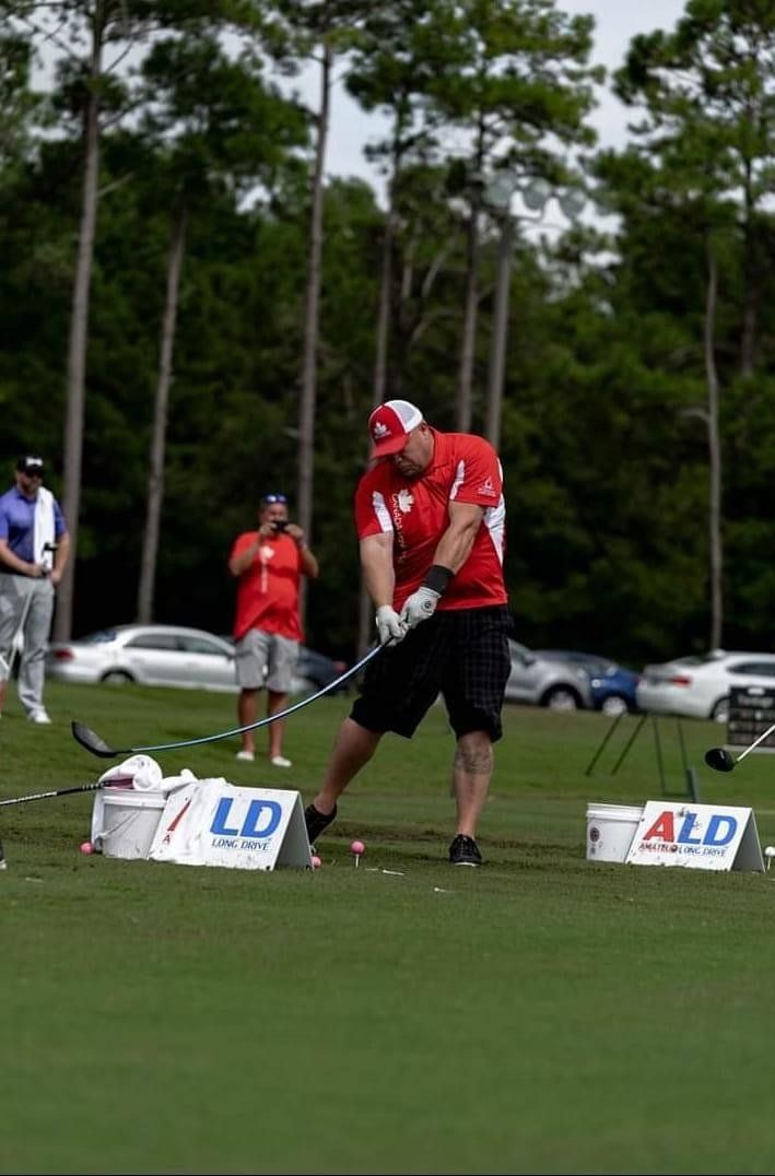 A man in a red shirt is swinging a golf club on a golf course