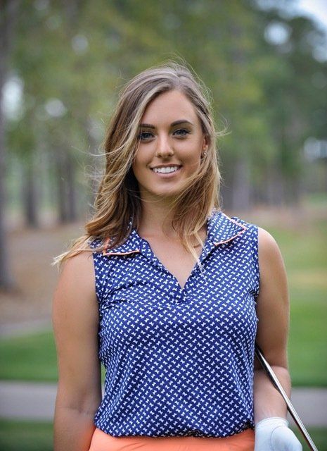 A woman is holding a golf club and smiling on a golf course.