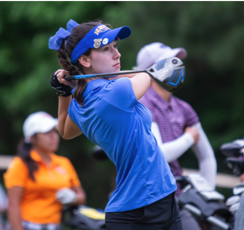 A woman in a blue shirt is swinging a golf club