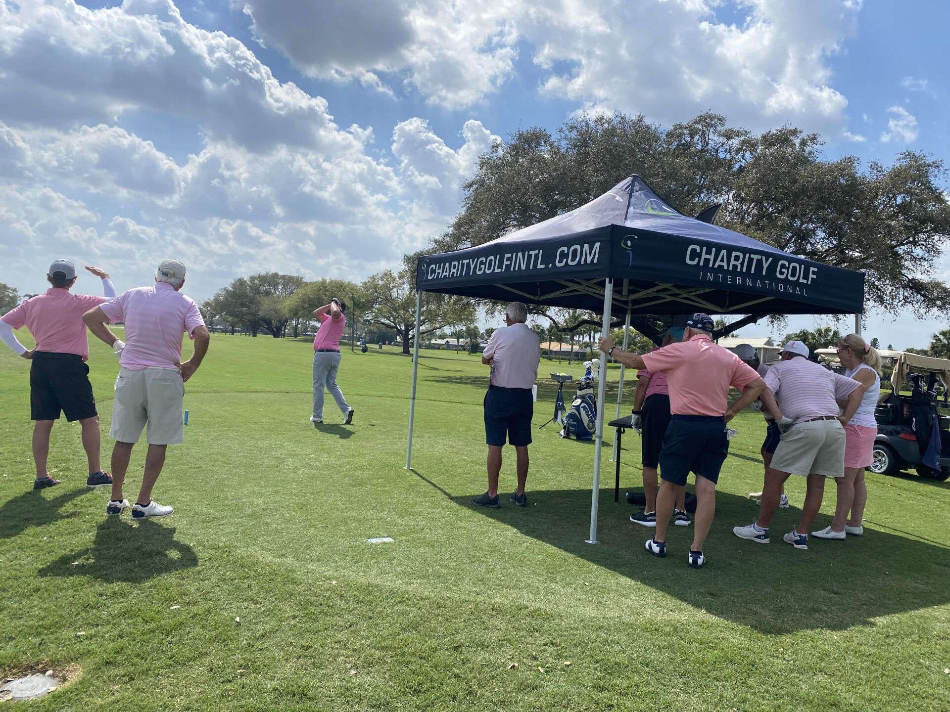 A group of people are standing under a tent on a golf course.