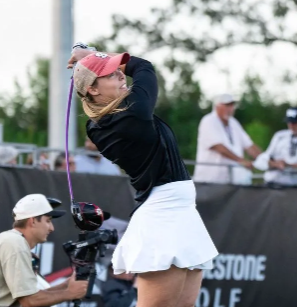 A woman is swinging a golf club in front of a banner that says bridgestone