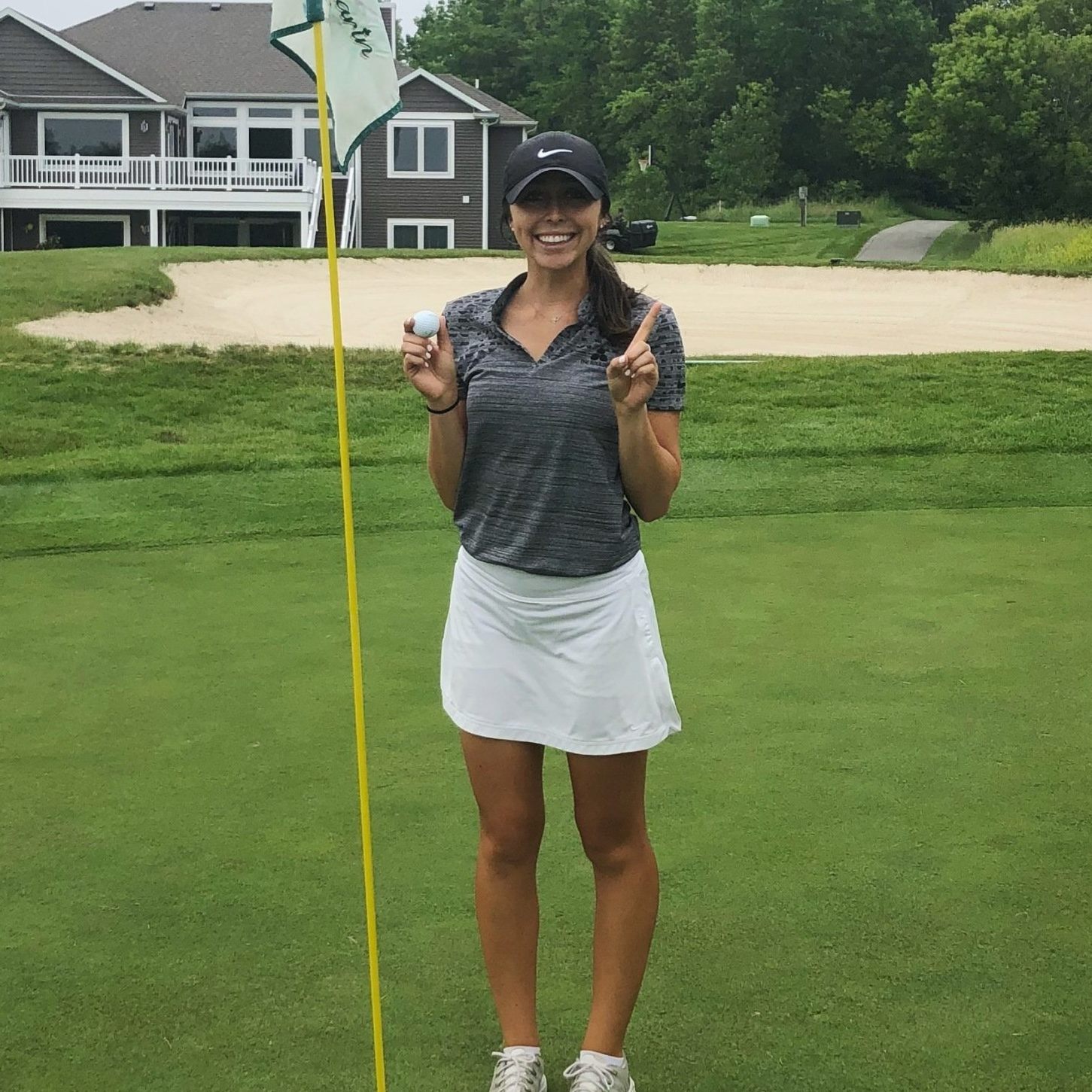 A woman is standing on a golf course holding a golf ball and a flag.